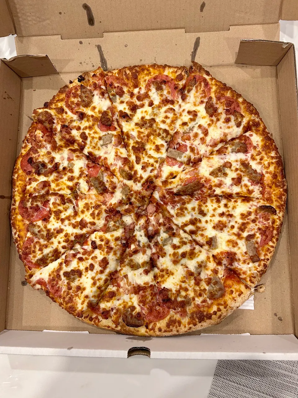 A whole, freshly baked pizza with pepperoni and sausage toppings, cut into slices and served in a cardboard delivery box.