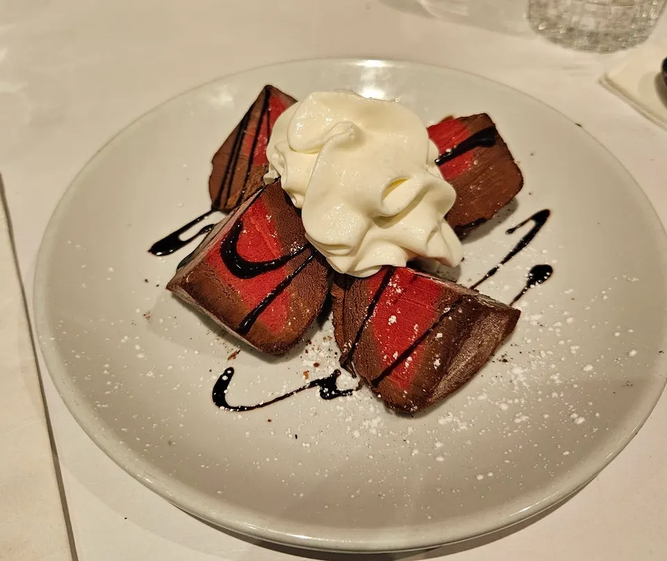 Four triangular slices of chocolate and raspberry tart arranged in a circle on a white plate, topped with a large dollop of whipped cream and drizzled with chocolate sauce.