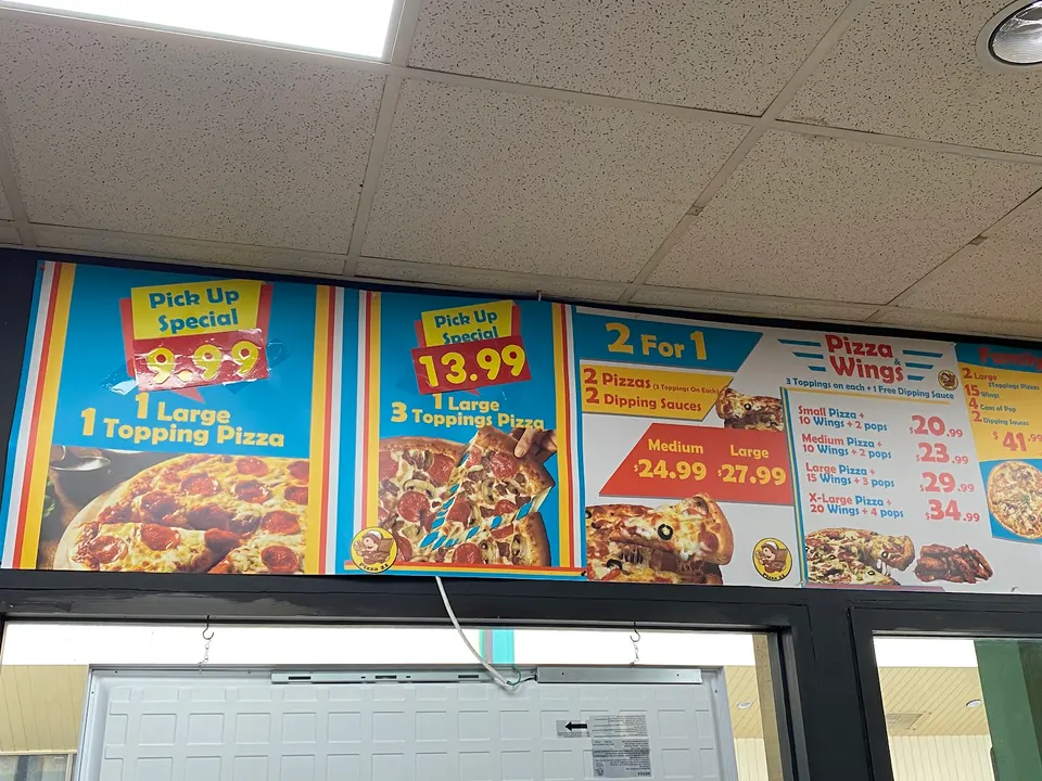 A colorful overhead menu board at Pizza 21 showing pick-up specials and combo deals for pizzas and wings.