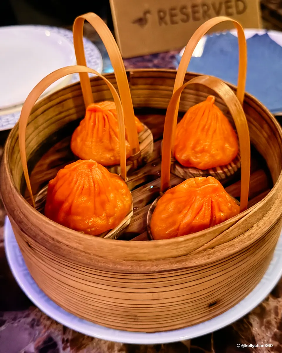 Four bright orange soup dumplings, each served in its own small basket with a tall handle, arranged inside a larger bamboo steamer basket.