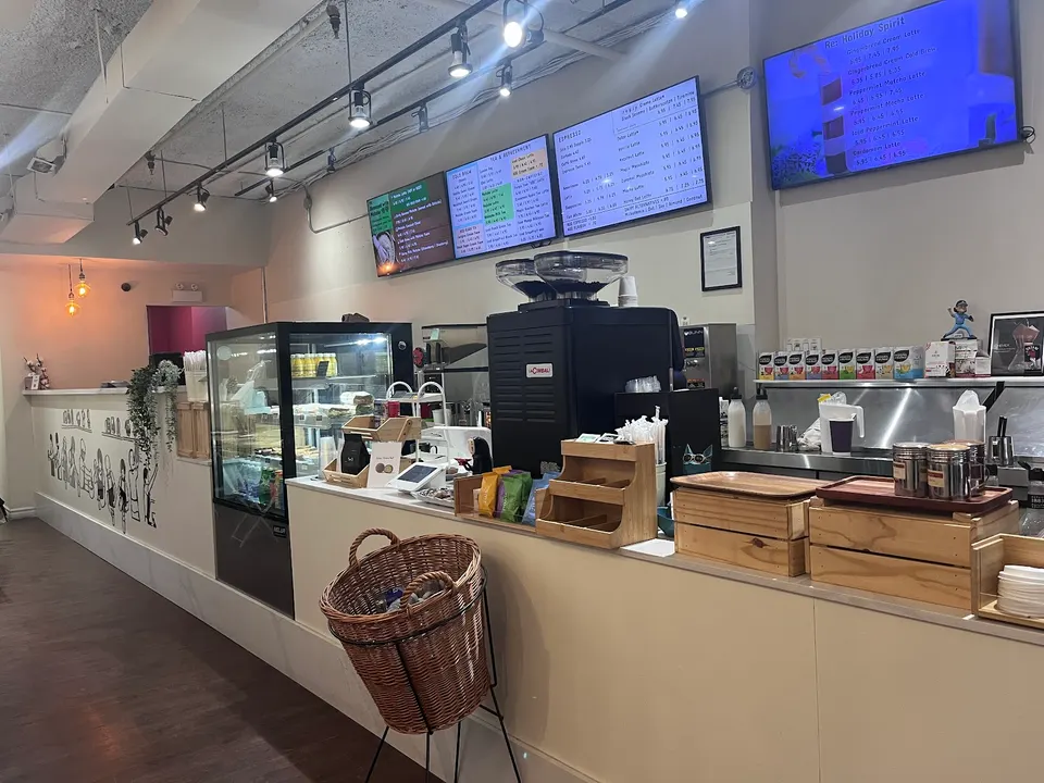 The service counter at Reply cafe, featuring a pastry display case, espresso machine, wooden organizers, and digital menu boards overhead.