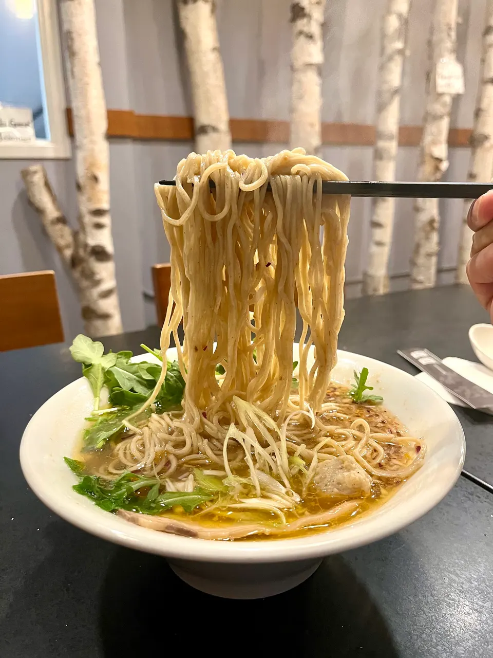 A close-up shot of a bowl of ramen with a large portion of noodles being lifted high out of the broth with chopsticks.