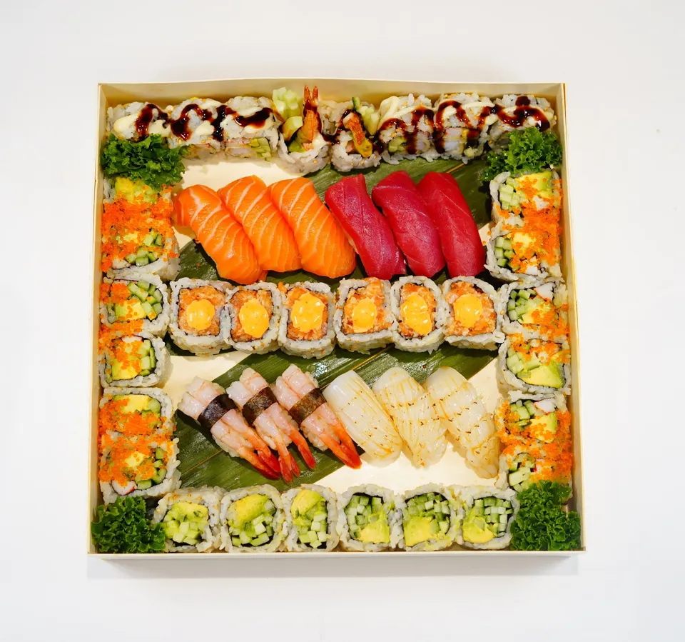 An overhead view of a square wooden bento box filled with an assortment of sushi, including salmon, tuna, and shrimp nigiri, alongside various maki rolls topped with orange tobiko and spicy mayo.