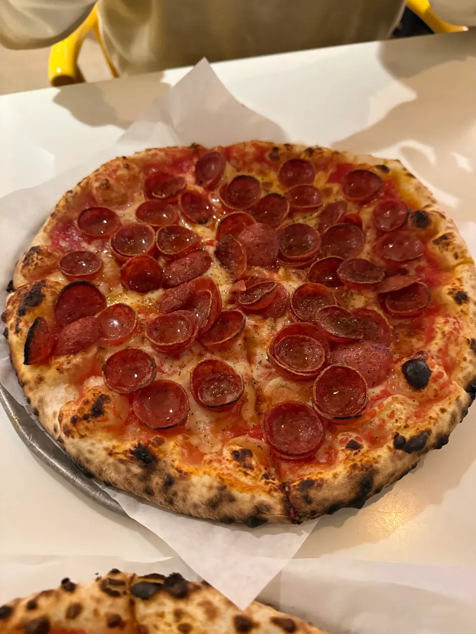 A freshly baked pepperoni pizza with a charred, bubbly crust, topped with melted cheese, tomato sauce, and numerous crispy, cupped pepperoni slices, served on parchment paper.