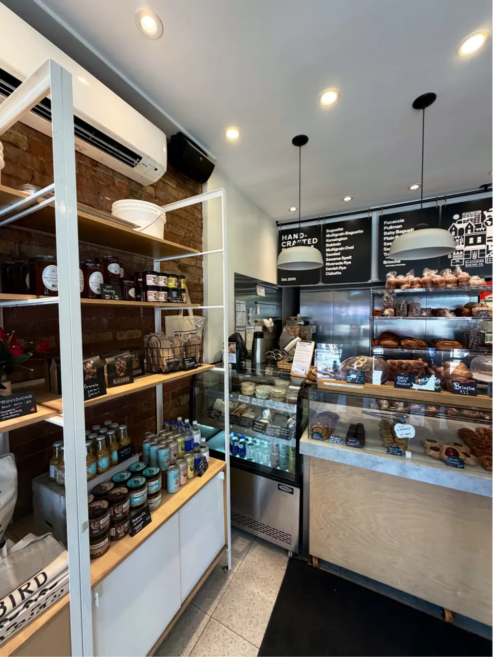 Interior of Blackbird Baking Co. in Kensington Market, showing a wooden counter with glass pastry displays, shelves stocked with packaged goods, and a menu board on the back wall.