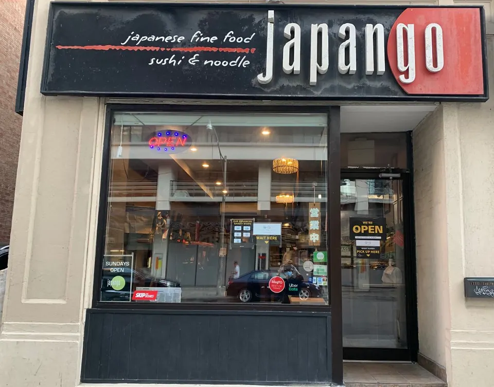The storefront of Japango restaurant, featuring a large black sign with white and red lettering, a large glass window showing the interior, and a glass entrance door with an open sign.