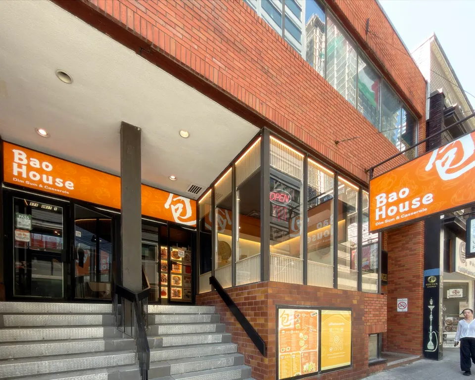 Exterior view of Bao House on Dundas Street, featuring a brick facade, orange signage, and steps leading up to the glass entrance doors.
