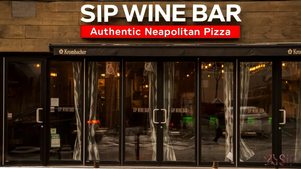 The exterior storefront of SIP Wine Bar, featuring a wooden facade, large glass folding doors with white curtains, and a red sign reading Authentic Neapolitan Pizza.