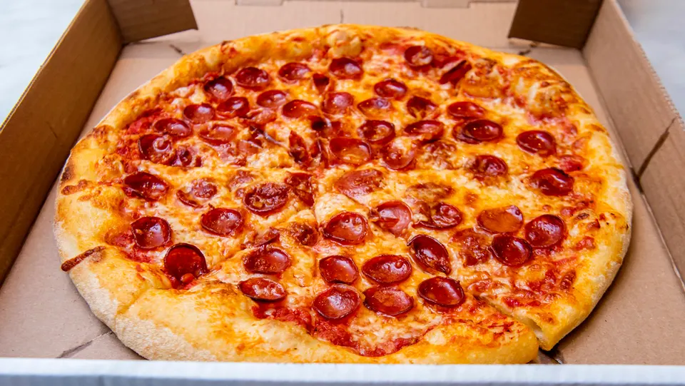 A whole pepperoni pizza with a golden-brown crust, melted cheese, and numerous pepperoni slices, presented inside a cardboard delivery box.