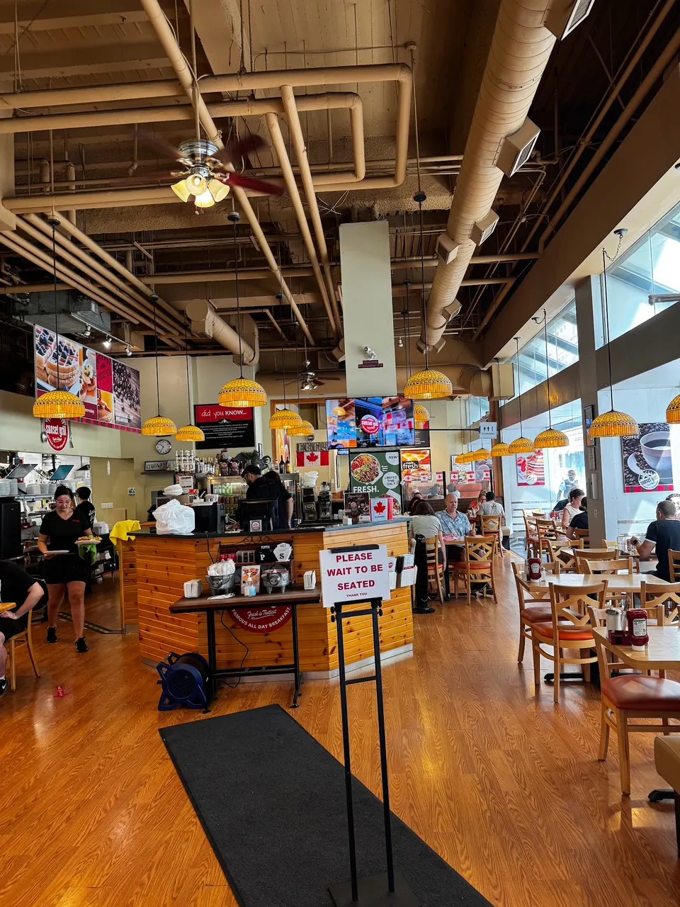 Interior of Sunset Grill restaurant featuring warm wood flooring, a central wooden counter, hanging yellow dome lights, and dining tables with patrons seated near large windows.