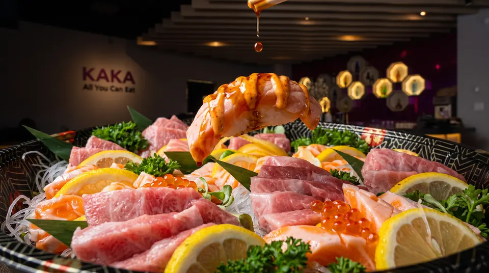 A close-up shot of a large sashimi platter with salmon, tuna, lemon slices, and parsley, featuring a piece of aburi salmon nigiri being held above with sauce dripping down.