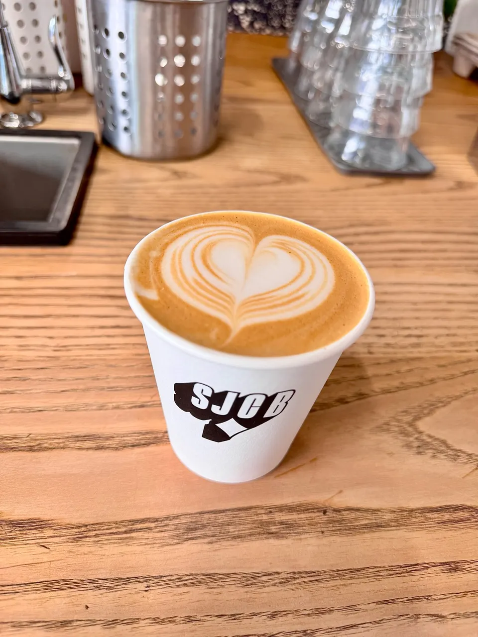 A paper cup of latte with heart-shaped latte art on a wooden counter at Robinson Bread.