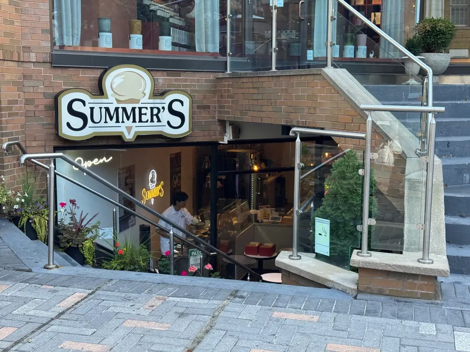 Exterior view of Summer's Ice Cream shop located down a short flight of stairs with a brick facade, glass railings, and a prominent sign featuring an ice cream cone logo.