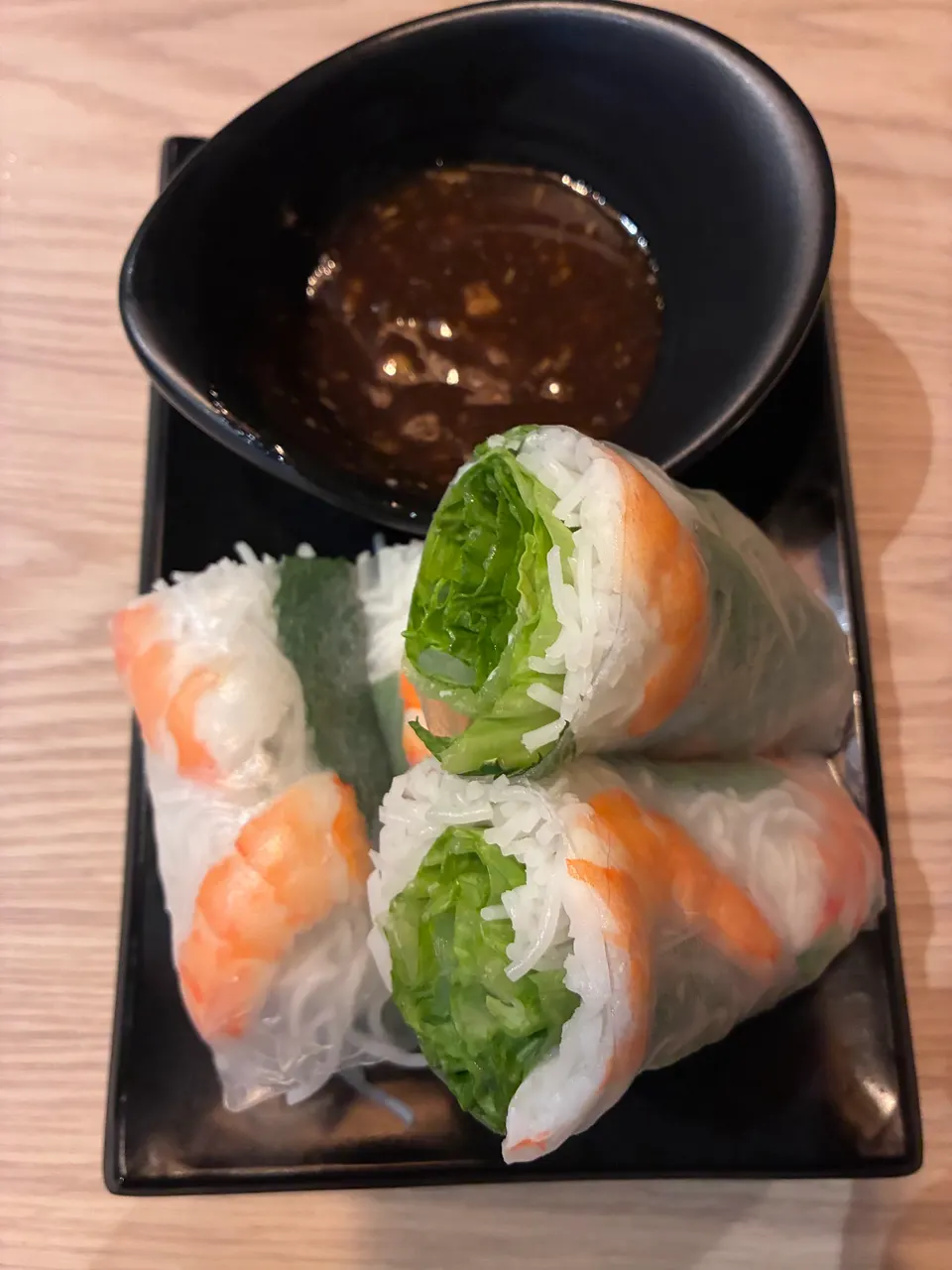 Vietnamese fresh spring rolls filled with shrimp, rice vermicelli, and lettuce, served on a black plate with a side of dark dipping sauce.