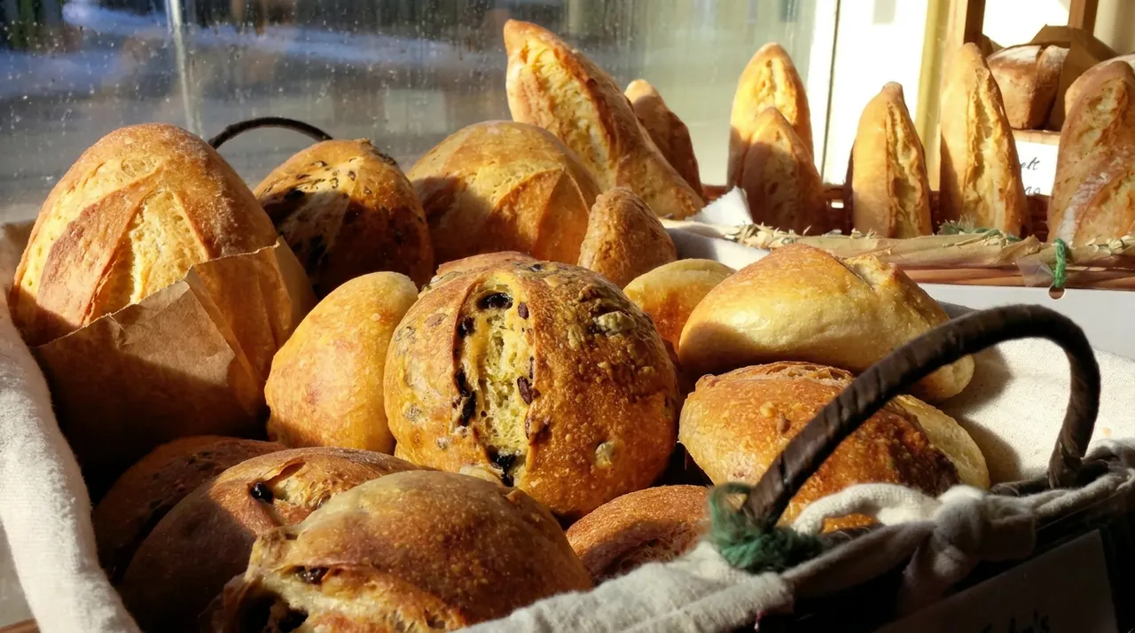 A basket filled with freshly baked artisanal bread loaves and rolls in a bakery window with warm sunlight streaming in.