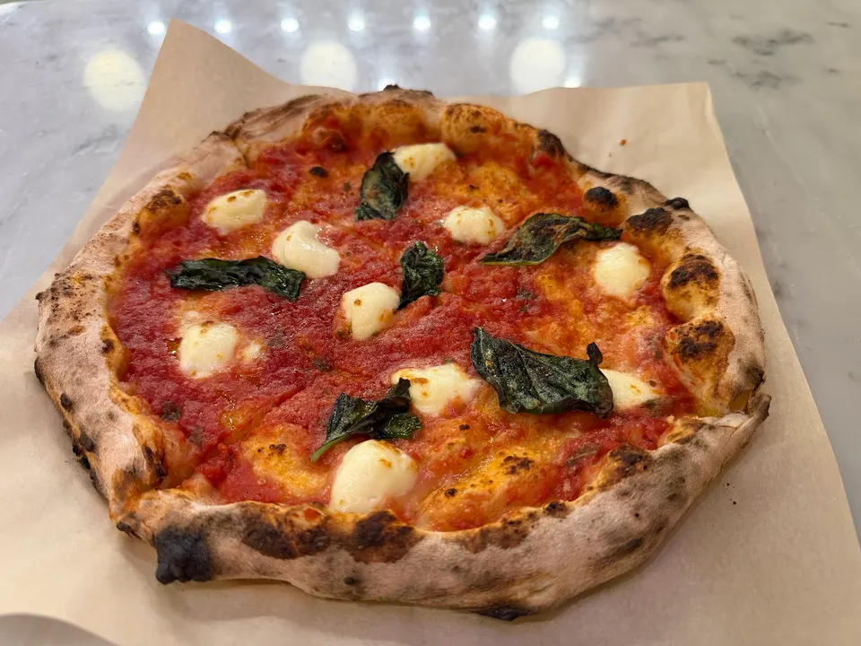 A freshly baked Neapolitan-style Margherita pizza with a charred crust, red tomato sauce, melted fresh mozzarella dollops, and green basil leaves on parchment paper.