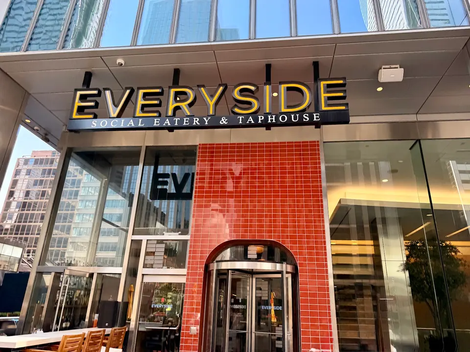 The exterior facade of Everyside Social Eatery & Taphouse, featuring a large black and yellow sign above a red tiled archway with a revolving glass door entrance.