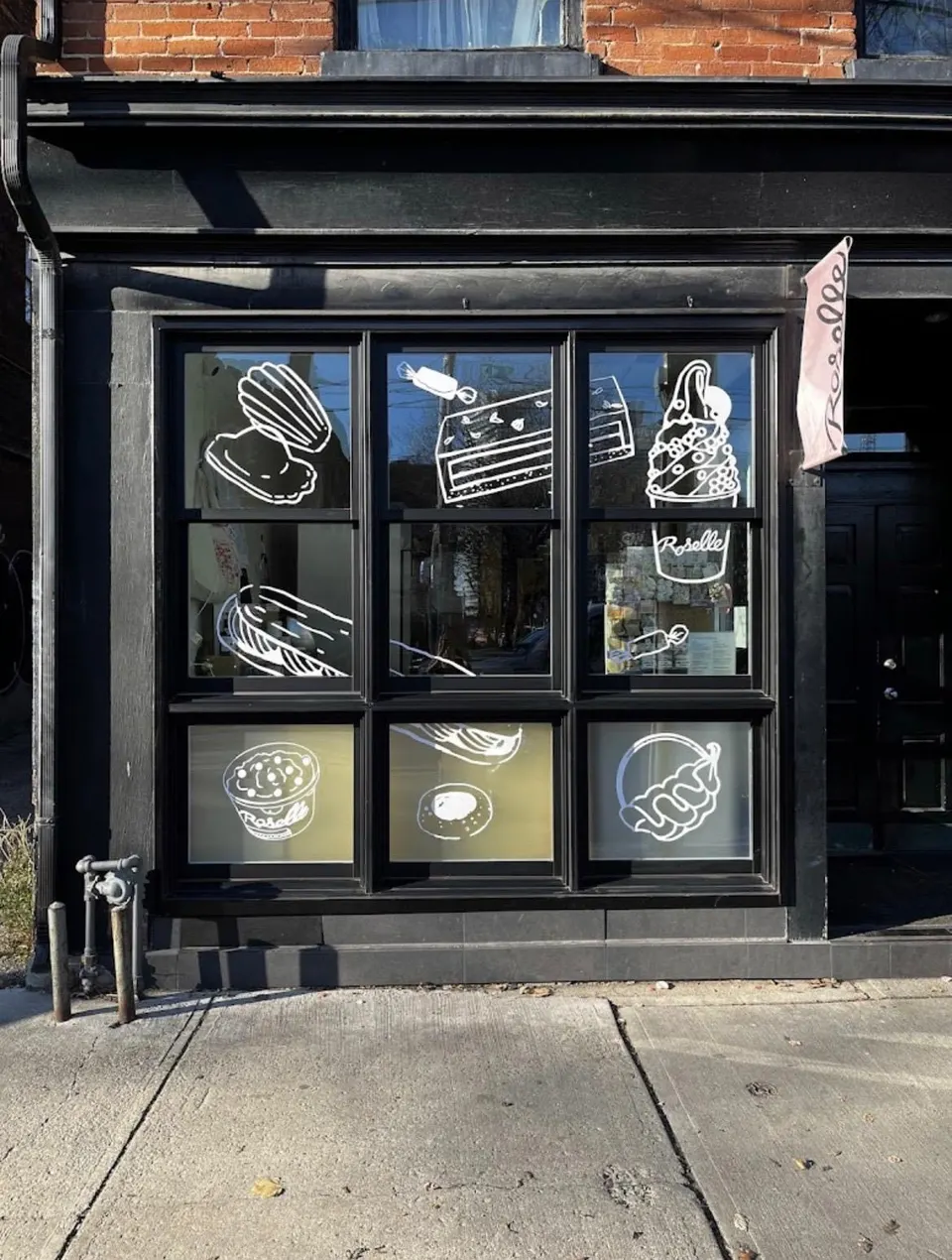 The black storefront of Roselle Desserts featuring large windows decorated with white line drawings of various pastries, cakes, and soft serve ice cream.