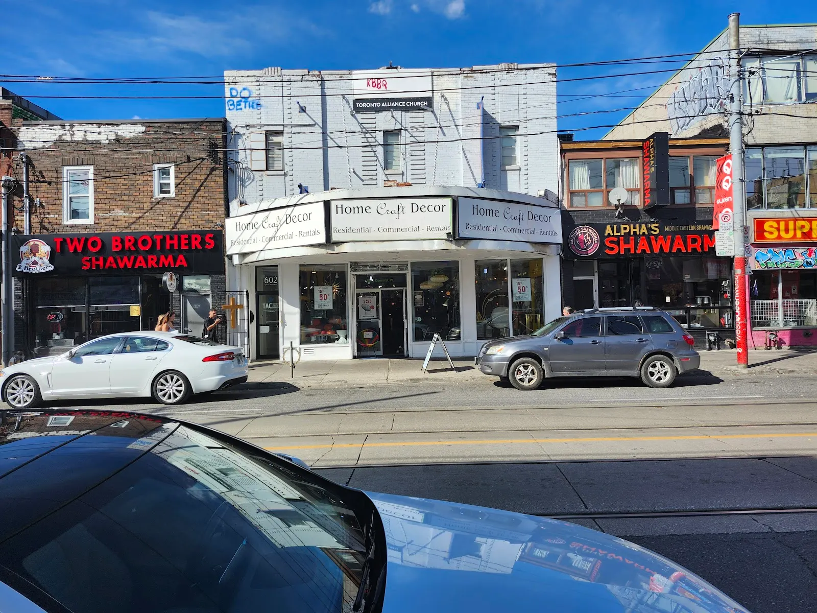 Exterior view of Alpha's Shawarma alongside neighboring storefronts on Queen Street West.