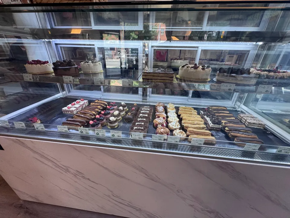 A glass display case filled with a variety of gluten-free cakes and pastries, including chocolate cakes, fruit tarts, eclairs, and small decorated desserts.