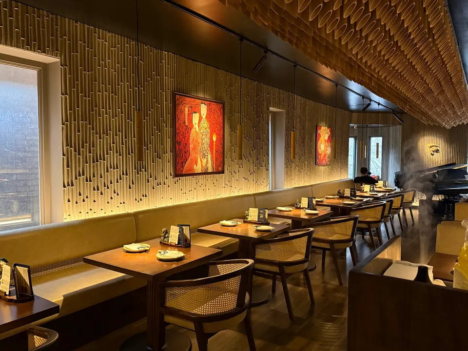 An elegant dining room at TRE - Viet Heritage Kitchen & Bar featuring a long banquette, wooden tables, woven-back chairs, and a textured bamboo-style wall with warm lighting and artwork.