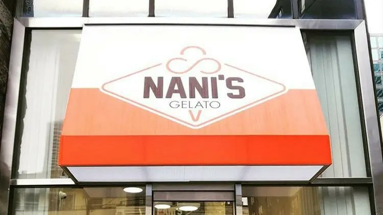 An outdoor awning sign for Nani's Gelato, featuring a white, orange, and red color scheme with a diamond-shaped logo containing the business name.