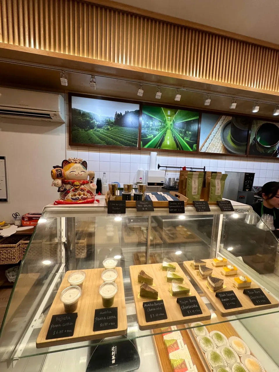 A glass display case at Tsujiri Dundas filled with Japanese desserts like matcha panna cotta, matcha basque cheesecake, and black sesame mousse cake on wooden trays.
