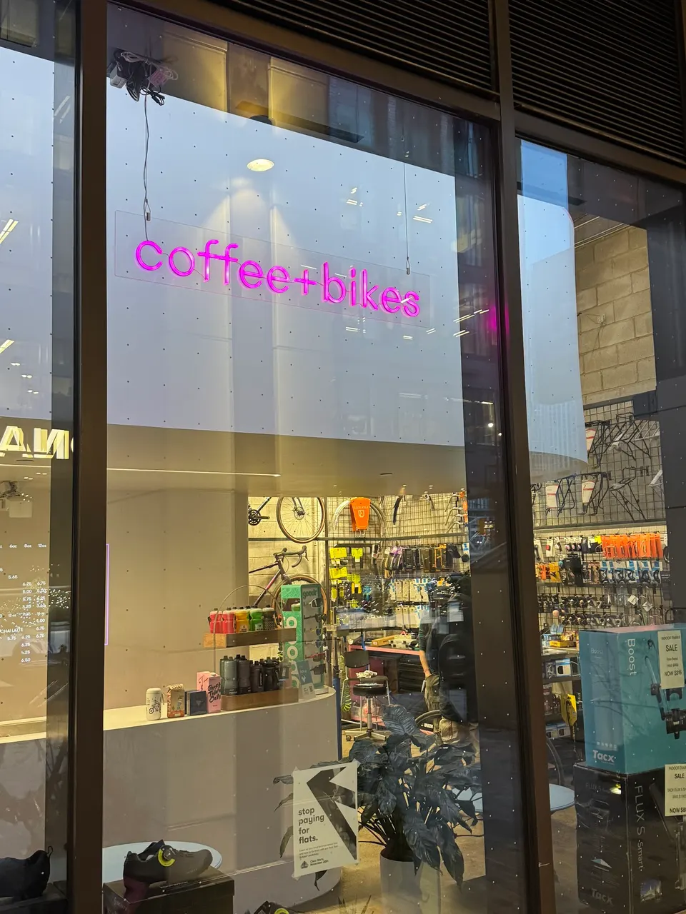 A storefront window of Fix Coffee + Bikes in Wellington Place, showing a bright pink neon sign that reads 'coffee+bikes' above a display of cycling gear and accessories.