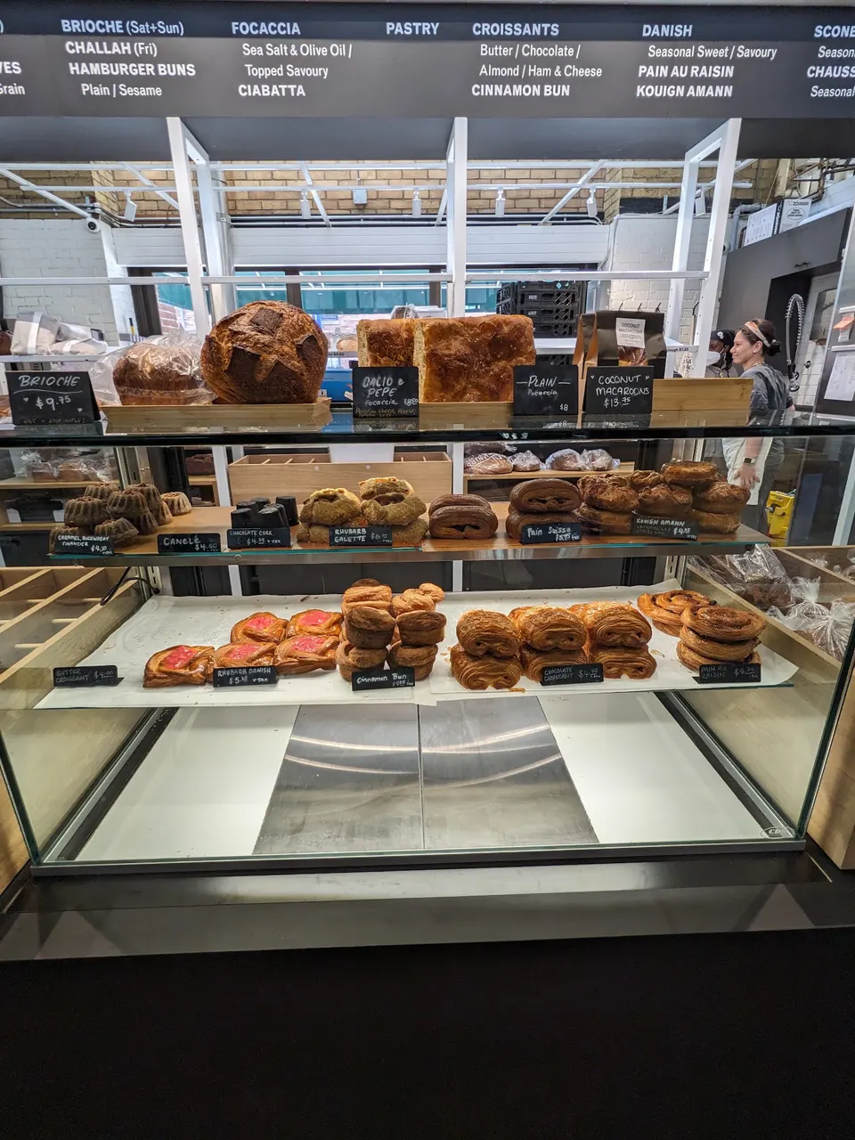 A glass display case filled with freshly baked goods at Blackbird Baking Co., featuring loaves of bread, focaccia, croissants, danishes, and other pastries with handwritten price tags.
