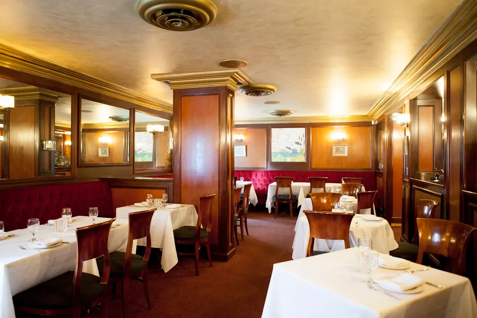 An elegant dining room at The Host Fine Indian Cuisine in Toronto, featuring white tablecloth-covered tables, polished wooden chairs, and plush red banquette seating under warm lighting.