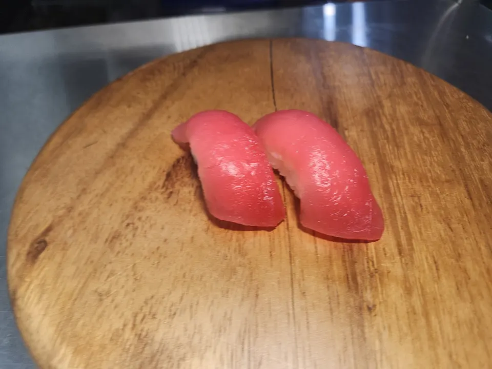 Two pieces of tuna nigiri sushi served on a round wooden platter.