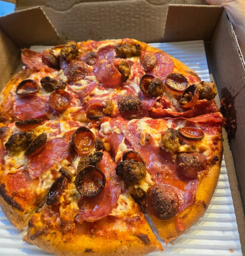 A freshly baked pizza with pepperoni and sausage chunks in a cardboard delivery box, sliced and ready to eat.
