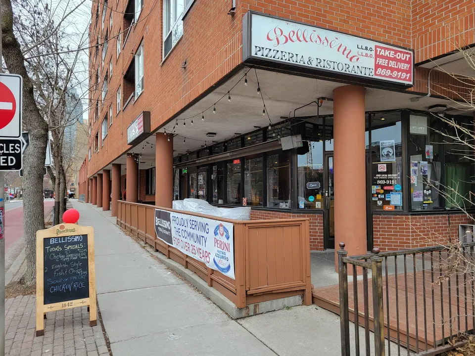 Exterior storefront of Bellissimo Pizzeria & Ristorante, featuring a brick building facade, outdoor patio railing, a sidewalk menu board, and a large overhead sign.