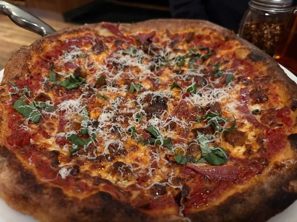 A freshly baked thin-crust pizza topped with tomato sauce, melted cheese, cured meats, fresh basil leaves, and a generous dusting of grated parmesan cheese.