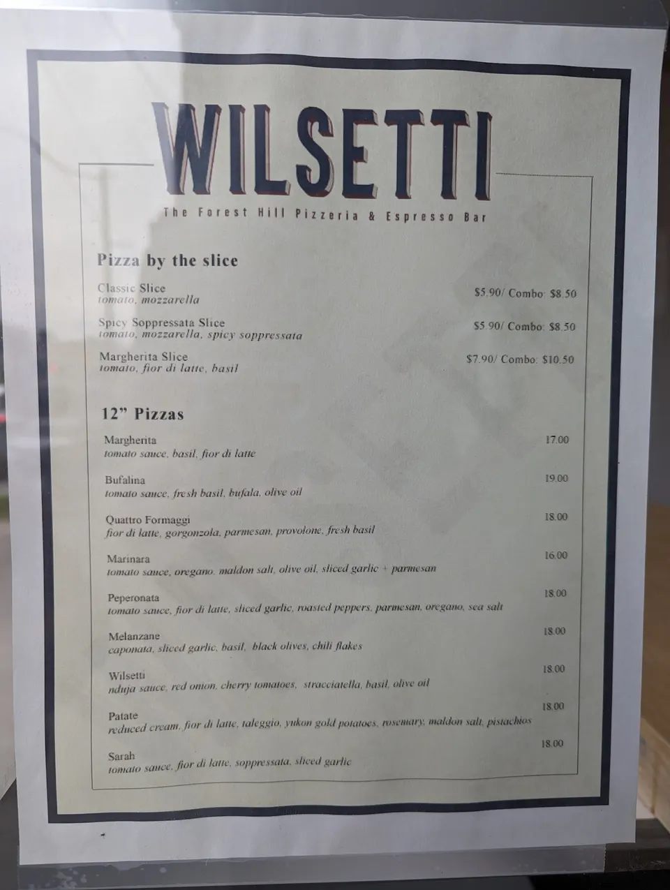 A printed menu for Wilsetti, The Forest Hill Pizzeria & Espresso Bar, showing sections for 'Pizza by the slice' and '12" Pizzas' with prices.