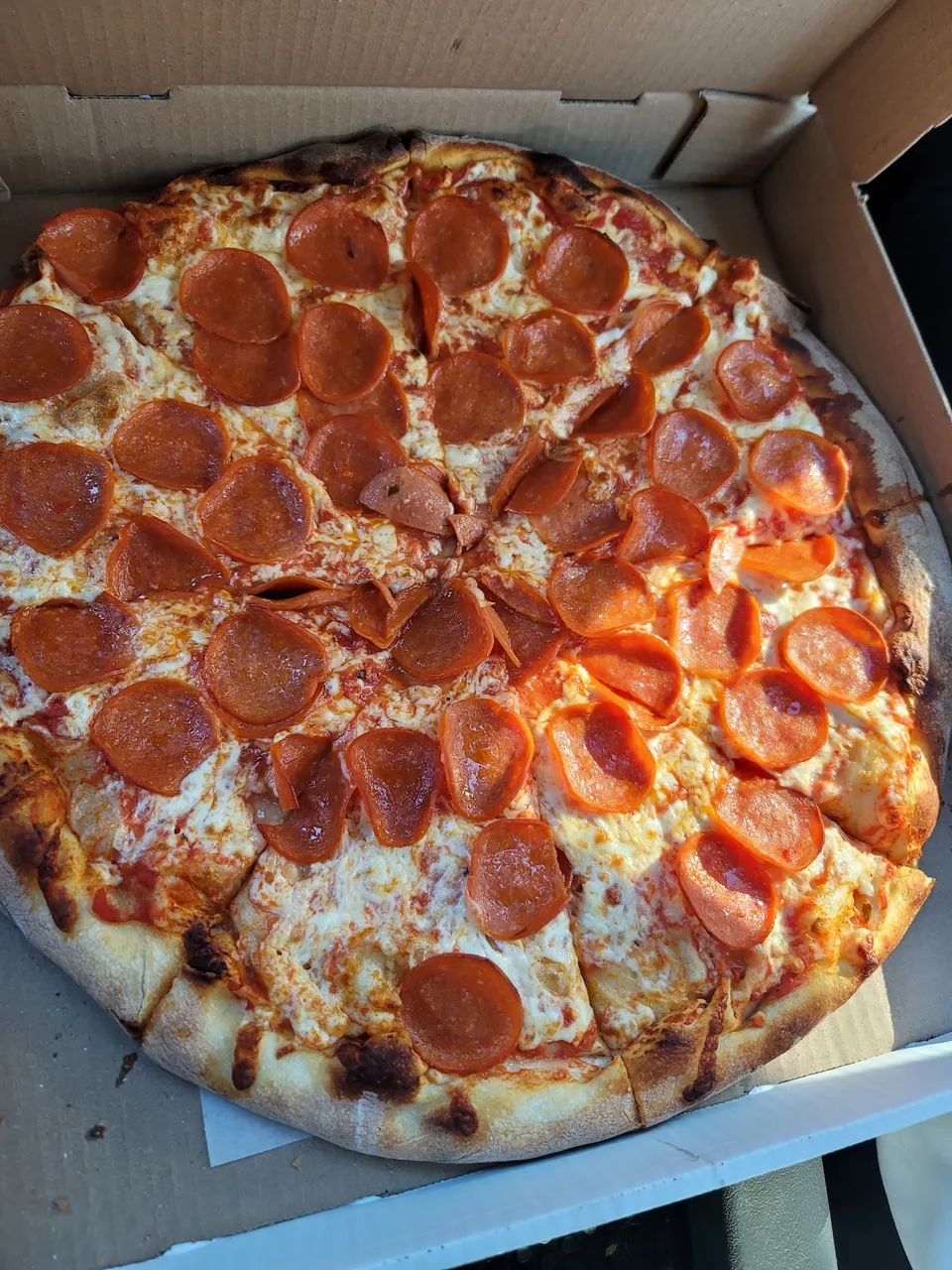 A whole pepperoni pizza with a golden-brown crust and melted cheese, sliced and served inside a cardboard delivery box.