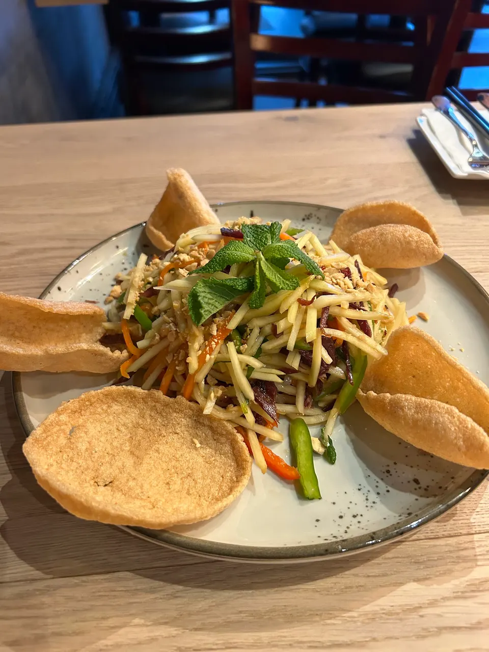 A Vietnamese salad with shredded green papaya, carrots, herbs, and crushed peanuts, served on a speckled plate with crispy shrimp crackers around the edges.