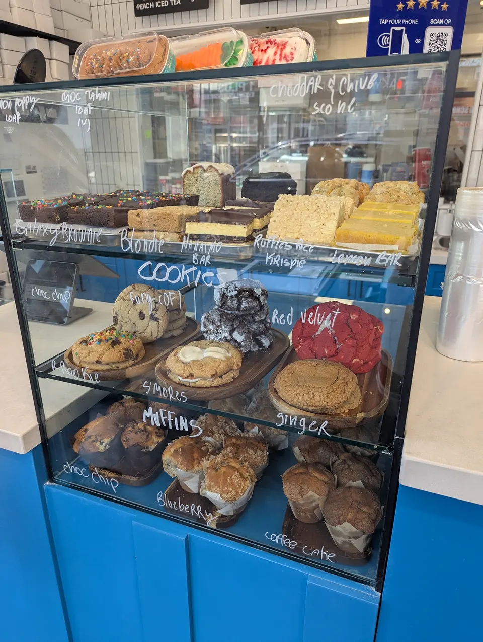 A glass display case at Wild Blue Bakery filled with baked goods including brownies, blondies, cookies, and muffins labeled with white handwriting.