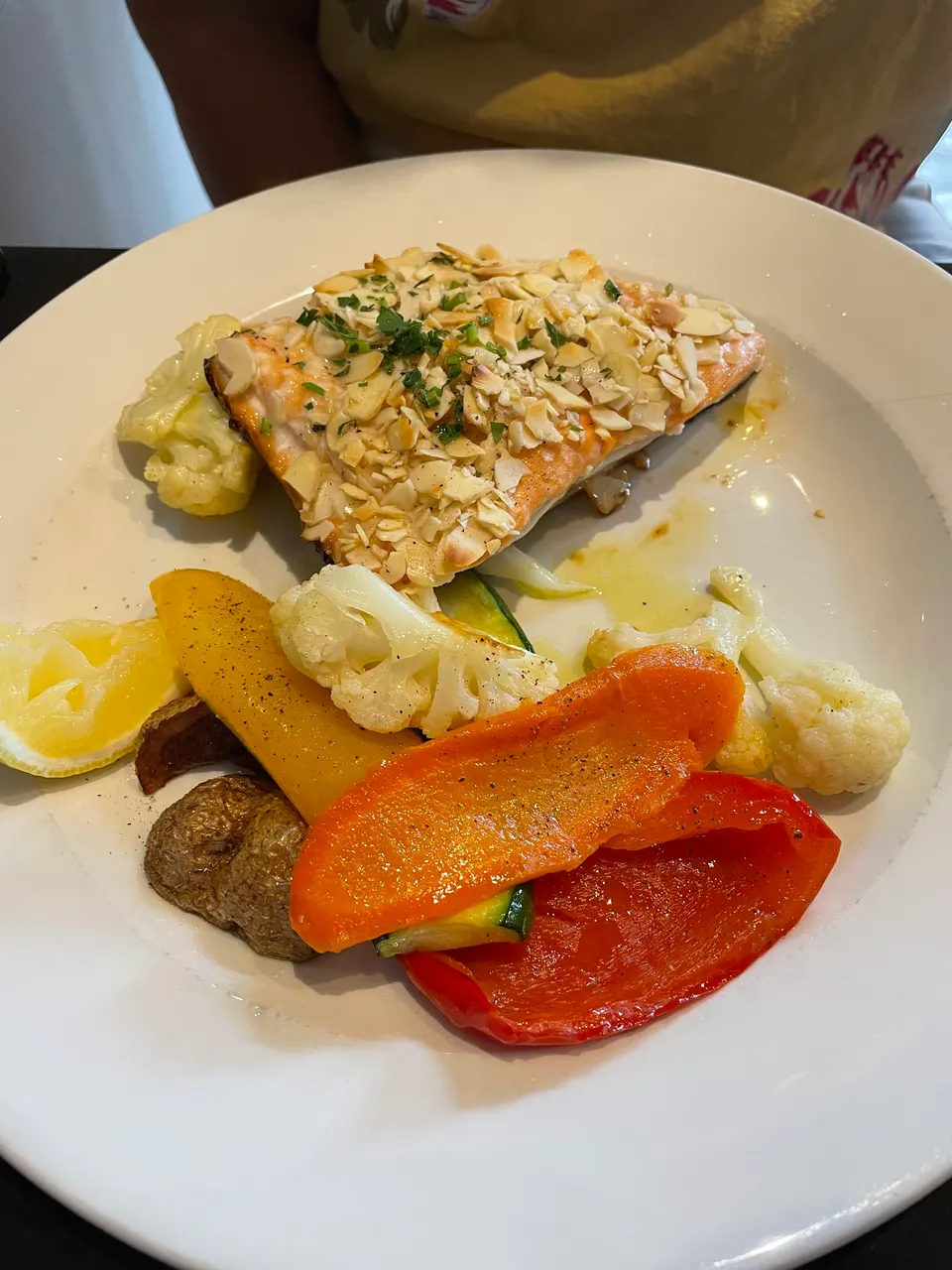A plate of almond-crusted salmon served with roasted vegetables including bell peppers, cauliflower, and zucchini, garnished with a lemon wedge.
