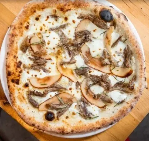 A freshly baked Neapolitan-style white pizza topped with sliced pears, melted mozzarella cheese, pulled meat, and fresh rosemary sprigs, served on a white plate over a wooden table.