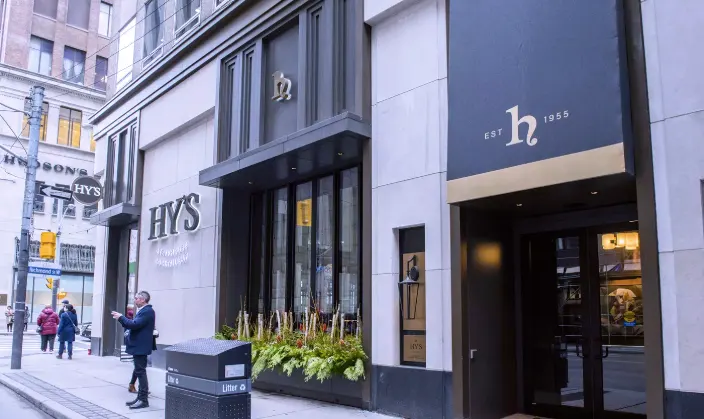 Exterior facade of Hy's Steakhouse & Cocktail Bar featuring a dark modern entrance with gold lettering, large windows with planter boxes, and a street view with pedestrians.
