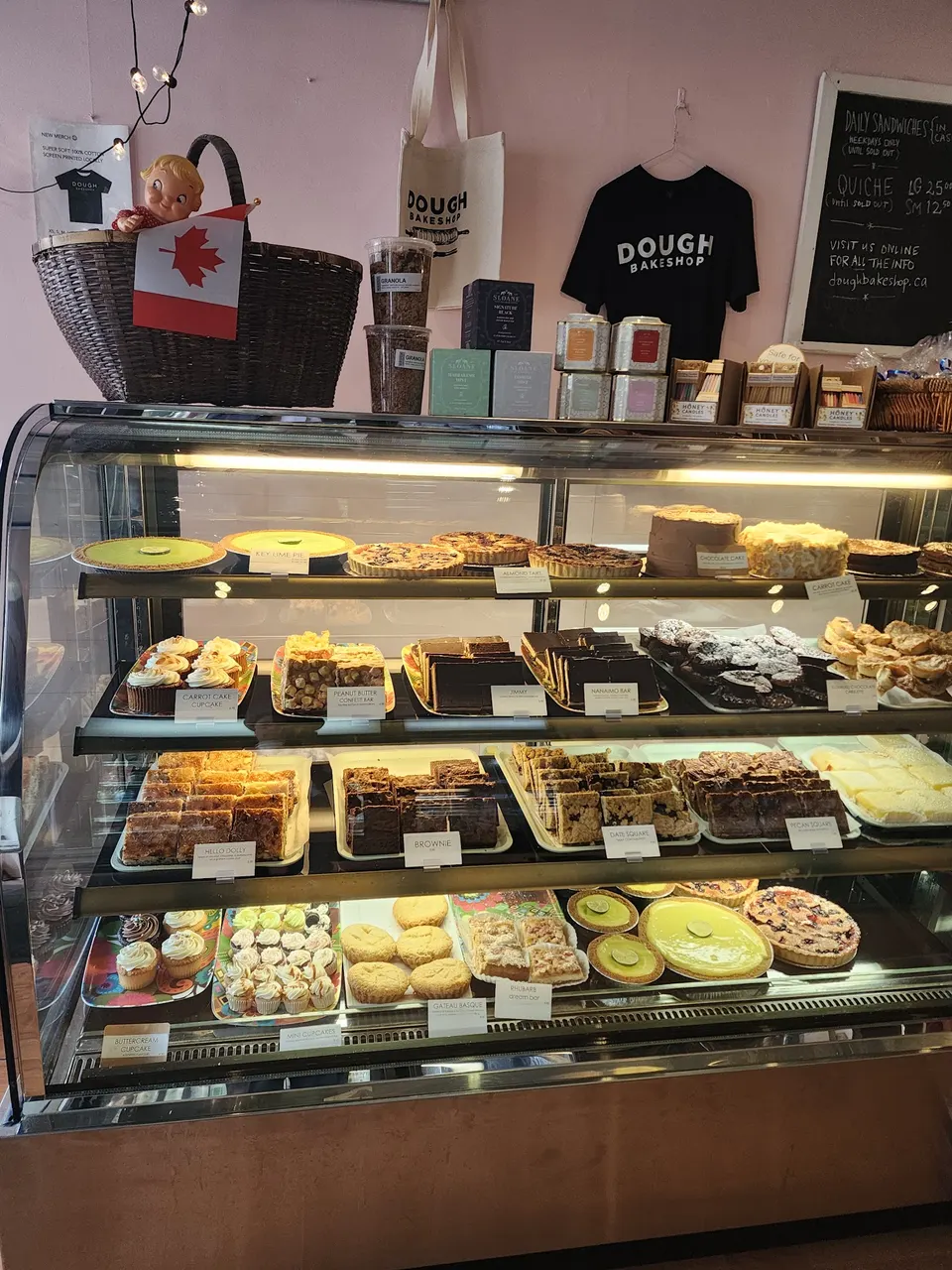 A glass display case at Dough Bakeshop filled with various baked goods including cupcakes, tarts, brownies, and cakes, with branded merchandise displayed on top.