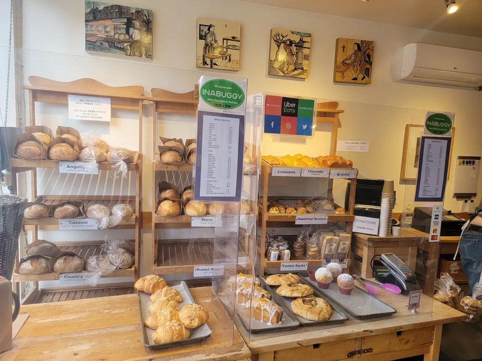 A bakery counter at St John's Bakery featuring wooden shelves stocked with fresh loaves of bread, croissants, and pastries, alongside a checkout area with payment terminals.