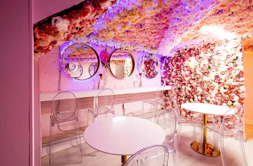 A pink-themed dining area with flower-covered walls and ceiling, round mirrors, clear acrylic chairs, and white tables.