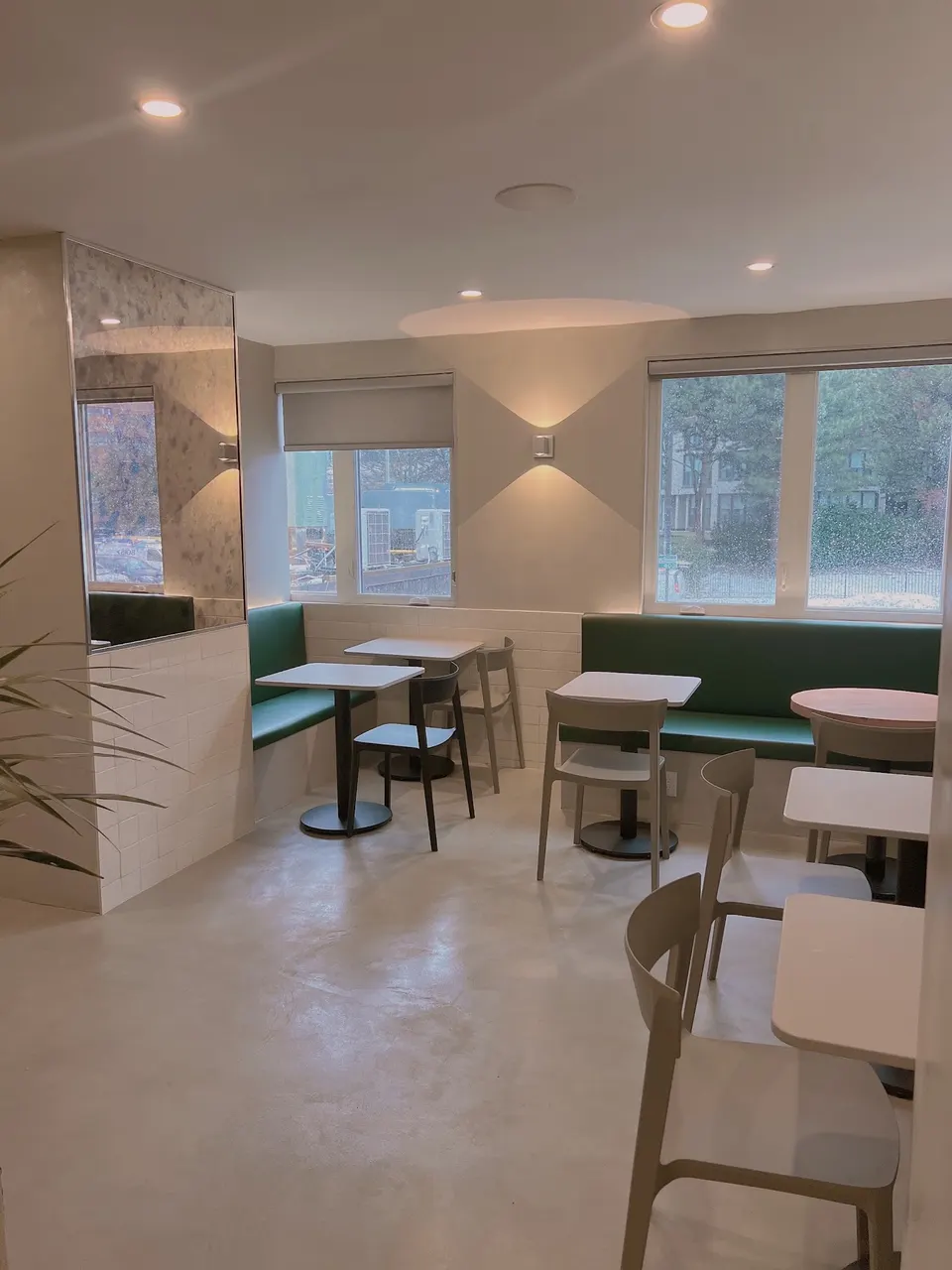 Interior of Cafe Kray featuring minimalist white tables, light grey chairs, and green banquette seating along the walls under warm lighting.