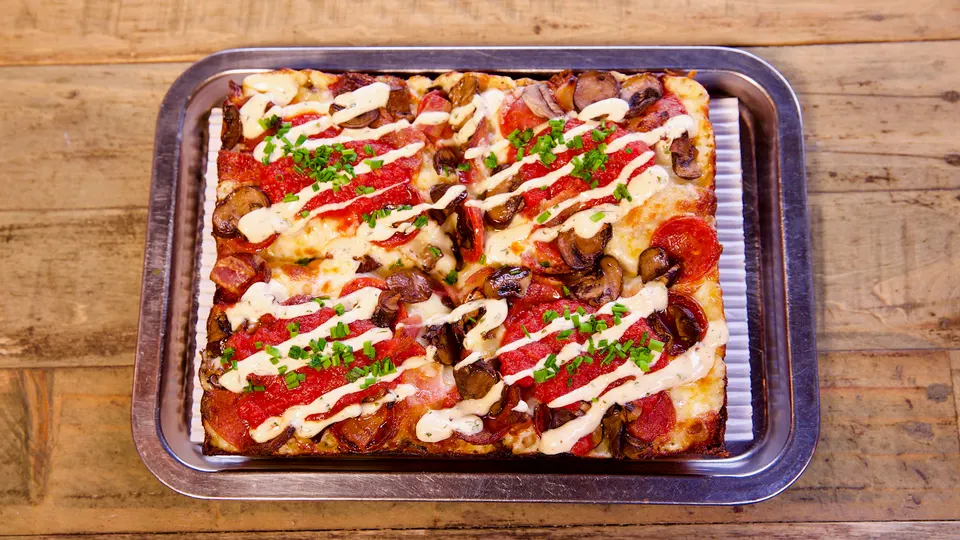A freshly baked Detroit-style square pizza topped with pepperoni, mushrooms, and savory drizzles.
