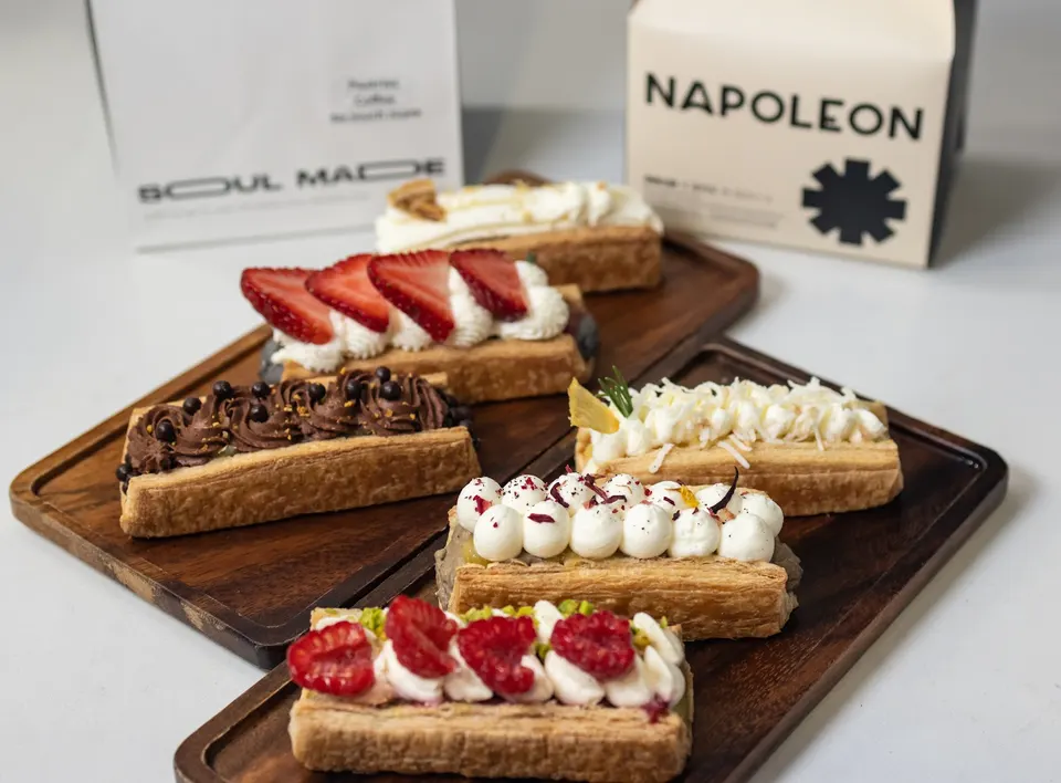 Six rectangular puff pastry desserts with various toppings like fresh strawberries, raspberries, chocolate cream, and white whipped cream, arranged on two wooden serving boards.