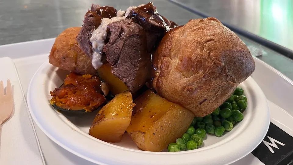 A roast dinner served on a white plate, featuring roast beef with gravy, a large Yorkshire pudding, roasted potatoes, peas, and other vegetables.