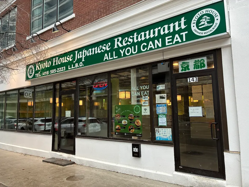 The exterior storefront of Kyoto House Japanese Restaurant, featuring a large green sign with white lettering, glass windows showing the interior, and a black-framed glass entrance door.