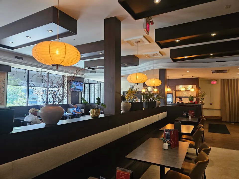 Interior of Yueh Tung Restaurant featuring dark wood booths, long banquette seating, modern tables, and warm orange paper lantern pendant lights hanging from the ceiling.
